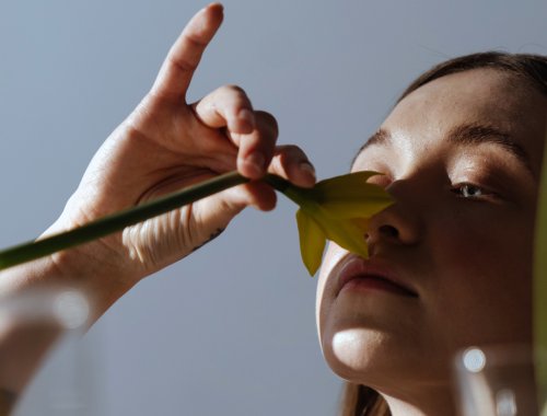 Mujer joven oliendo una flor.