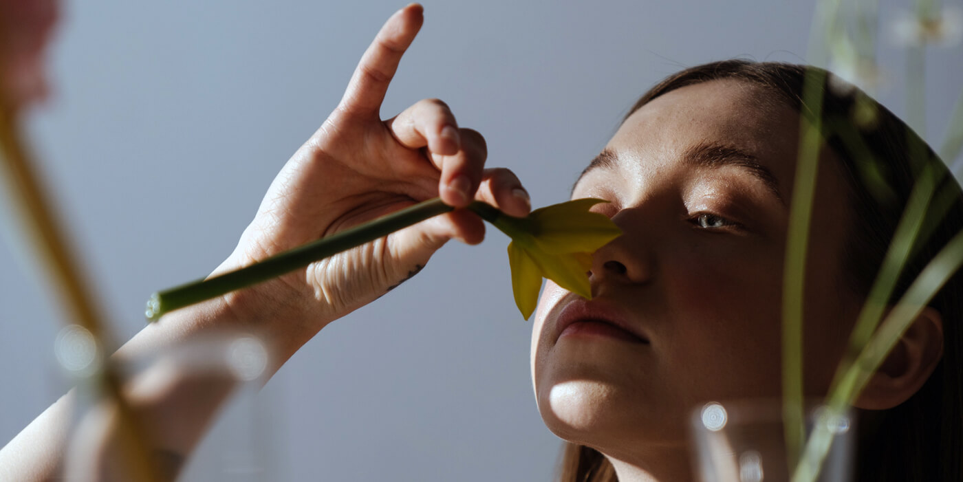 Mujer joven oliendo una flor.