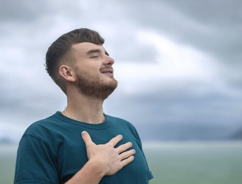 Joven en mitad de la naturaleza, respirando con una mano en el pecho