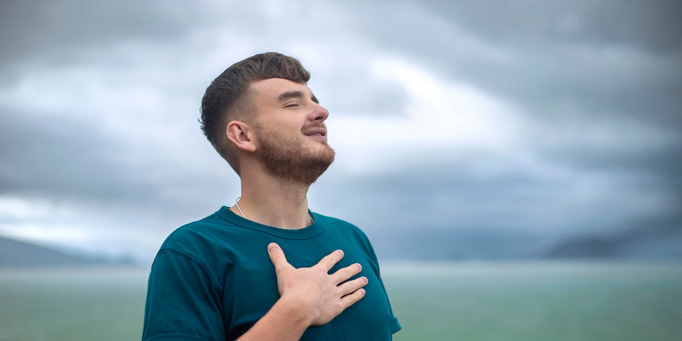 Joven en mitad de la naturaleza, respirando con una mano en el pecho