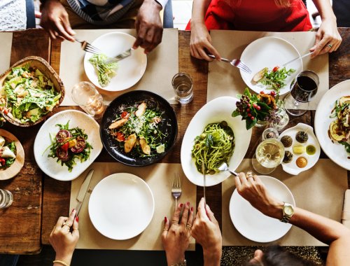 plano cenital de diversas personas sentadas a la mesa, sirviéndose comida en sus platos.