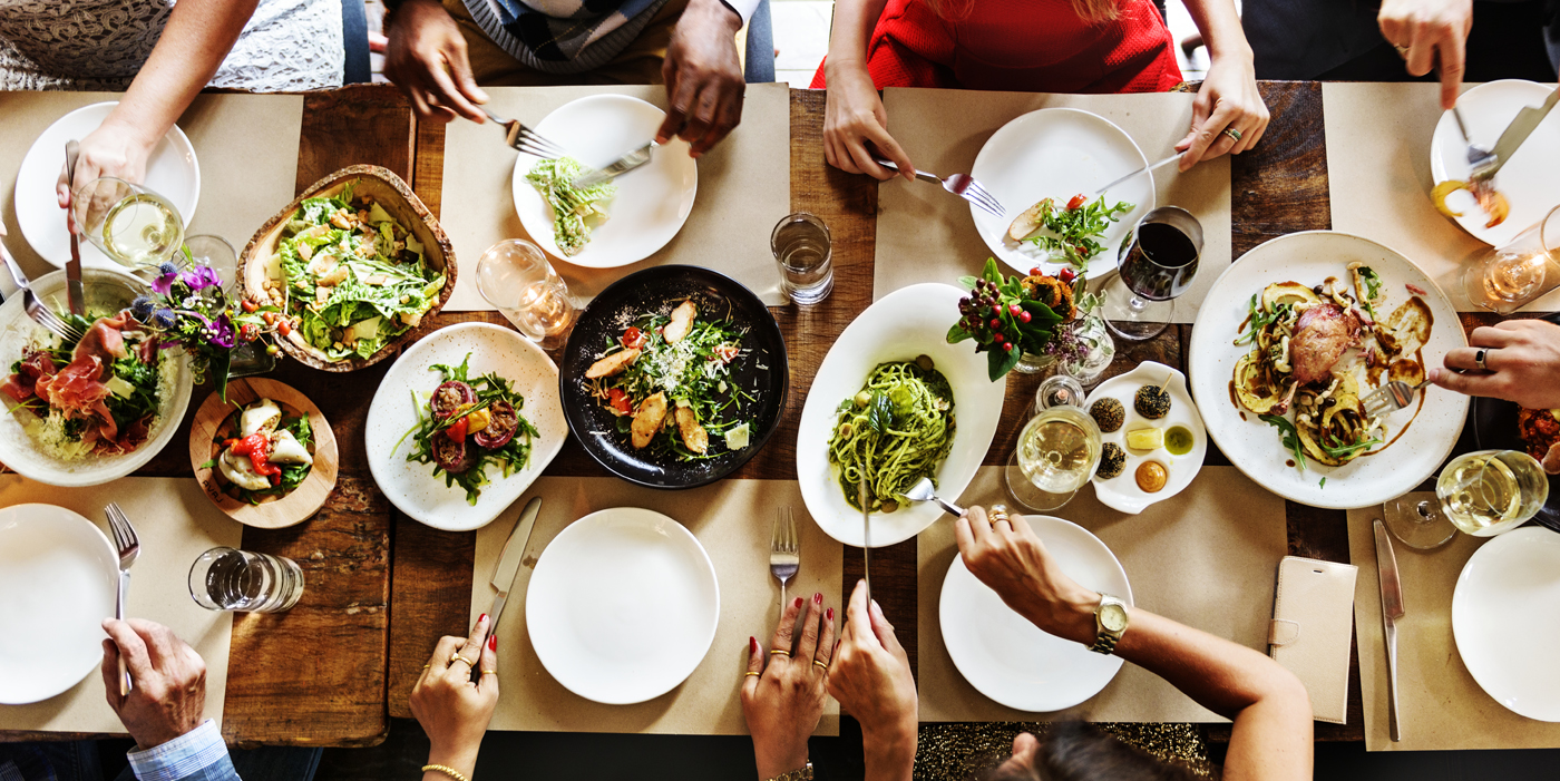 plano cenital de diversas personas sentadas a la mesa, sirviéndose comida en sus platos.