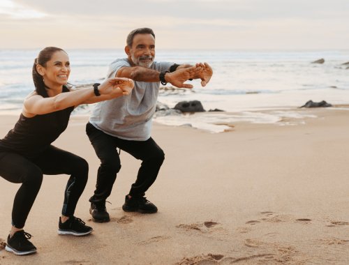 Pareja de seniors haciendo sentadillas en la playa.