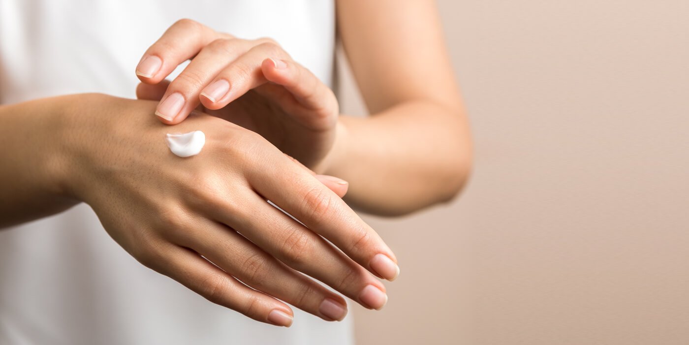 Mujer aplicándose crema en una mano