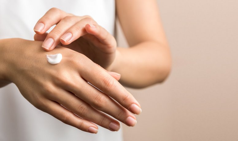 Mujer aplicándose crema en una mano